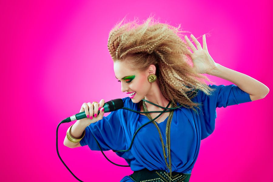 Portrait of 1980s style happy young woman dancing and singing into microphone.
