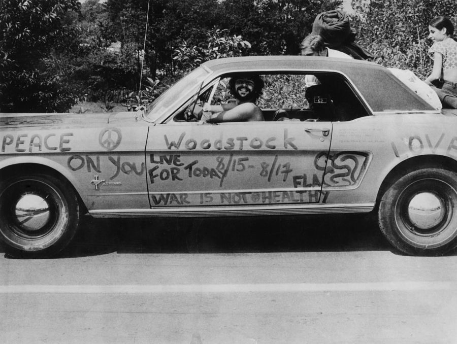 A music fan at Woodstock pop festival in his car covered in anti-war slogans for love and peace.  Photographer: Three Lions/Getty Images