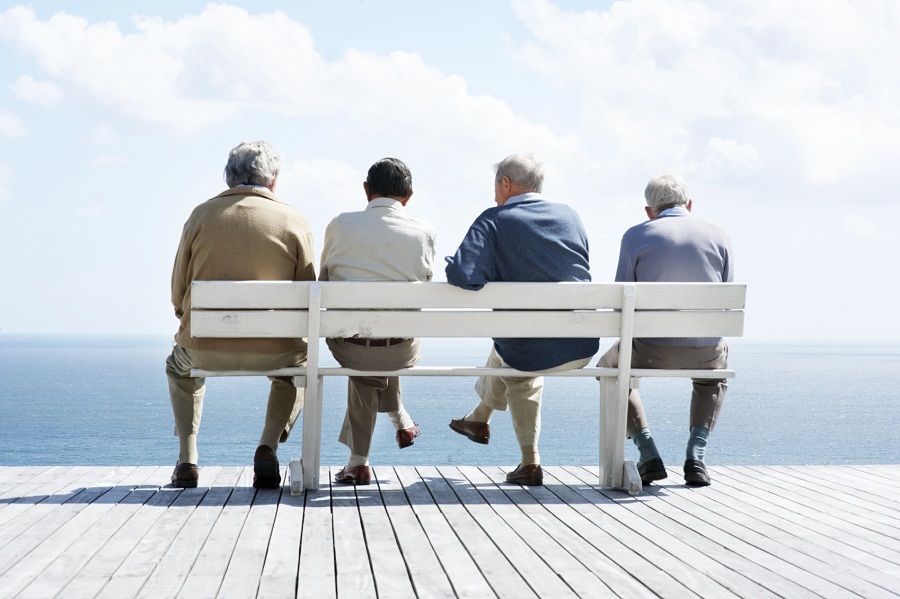 Rear view of group of old male friends sitting together on bench by the ocean - Outdoor