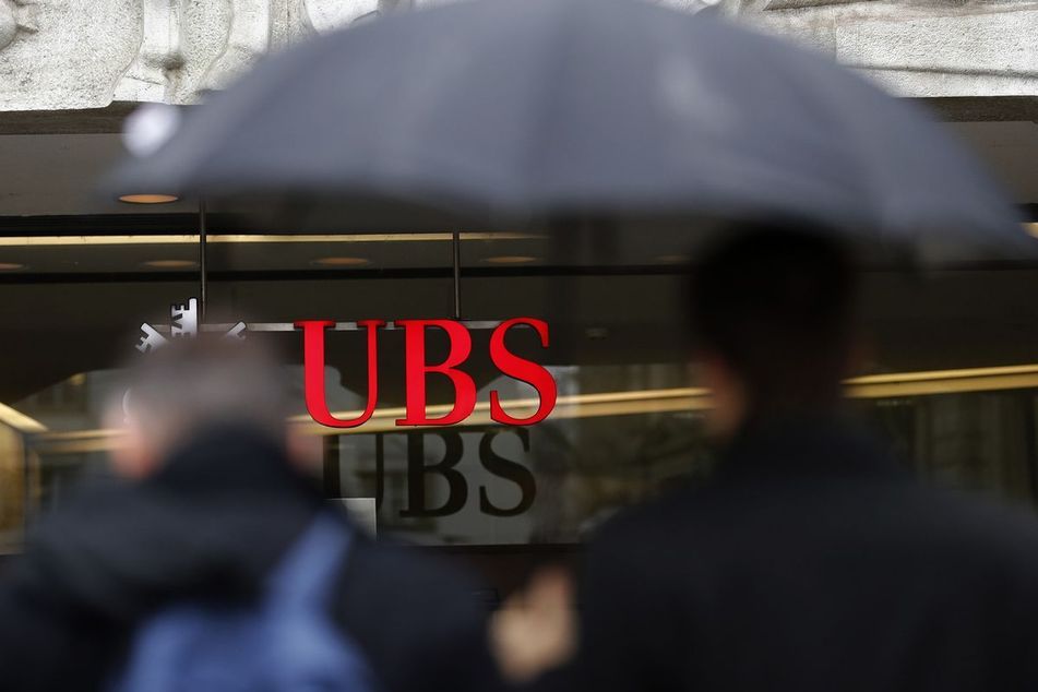Man under an umbrella passing UBS sign