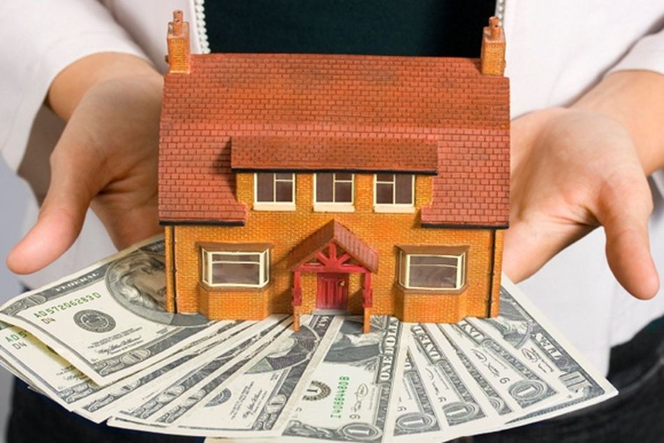 man-holding-toy-house-atop-array-of-dollar-bills