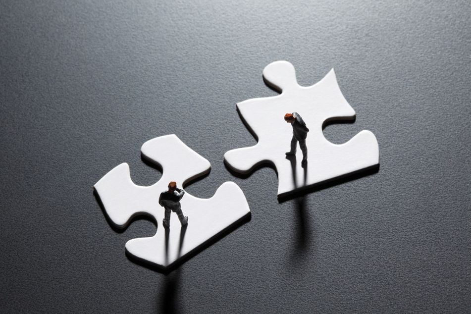 Two-tiny-men-standing-on-puzzle-pieces-shaking-hands