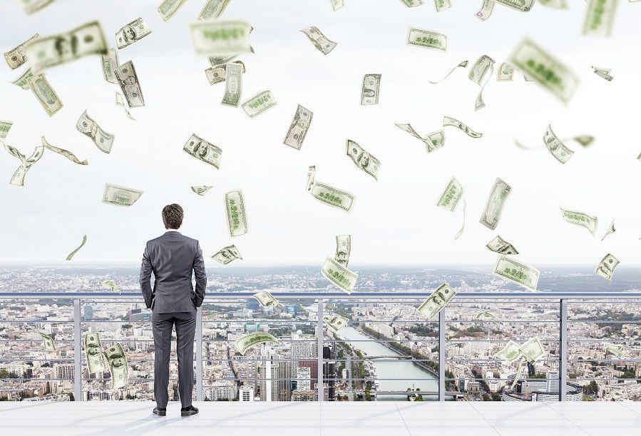 Young businessman with hands in pockets standing on the roof of a business centre and looking at New York. Money falling from above. Back view. Concept of earning money.