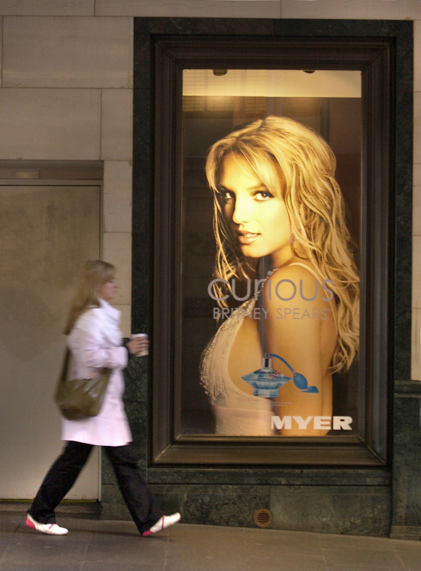 A woman walks by an advertisement showing singer Brittany Spears on display at a Coles Myer department store in Sydney, Australia on Tuesday 12 July, 2005. Coles Myer Ltd., Australia's biggest retailer, agreed to sell its Myer department stores to a group led by buyout firm Newbridge Capital LLC for A$1.4 billion ($1 billion) to focus on its larger supermarkets business.  Photographer: Jack Atley/Bloomberg News