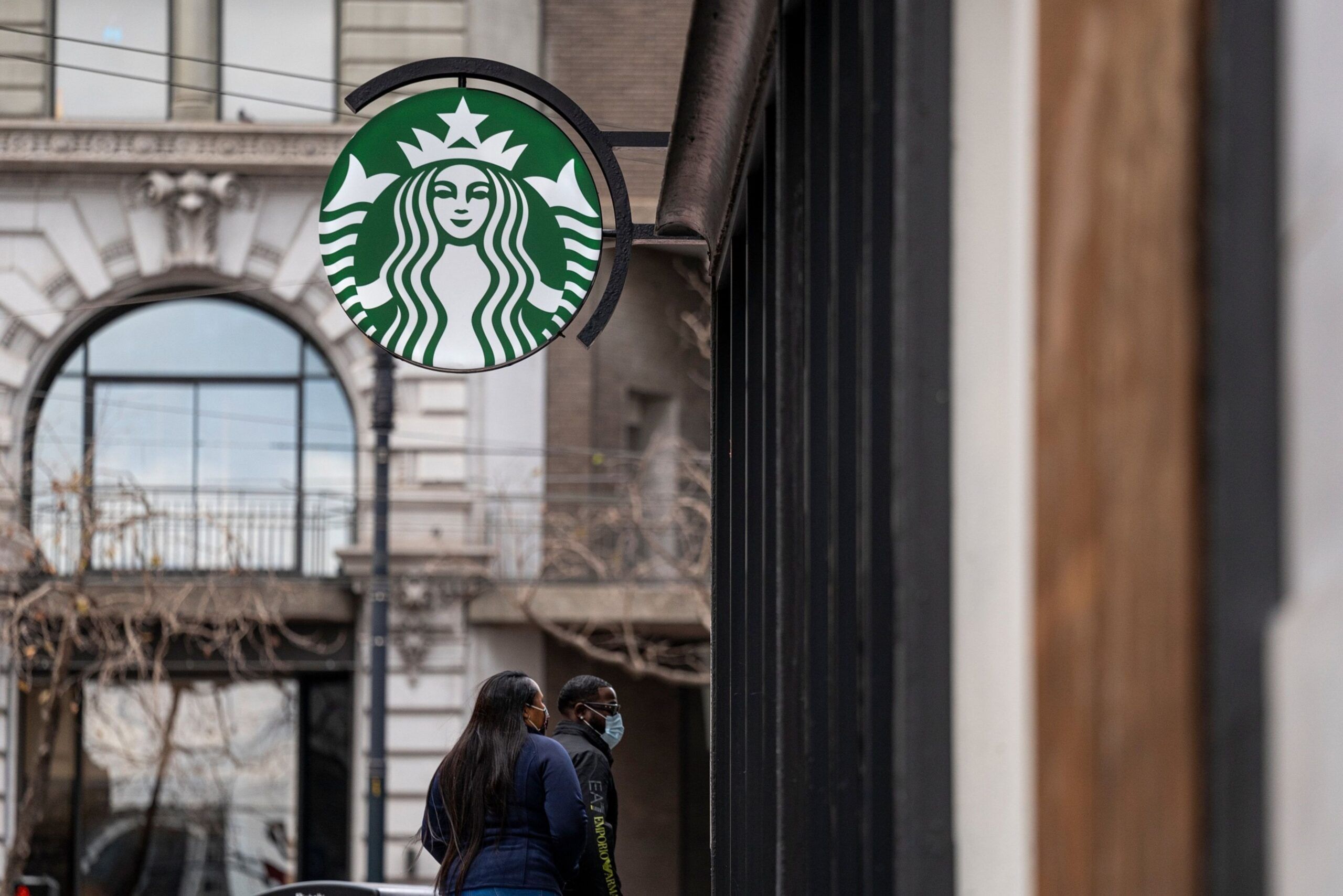Pedestrians wearing protective masks walk past a Starbucks coffee shop in San Francisco, California, U.S., on Thursday, Jan. 21, 2021. Starbucks Corp. is expected to release earnings figures on January 26. Photographer: David Paul Morris/Bloomberg
