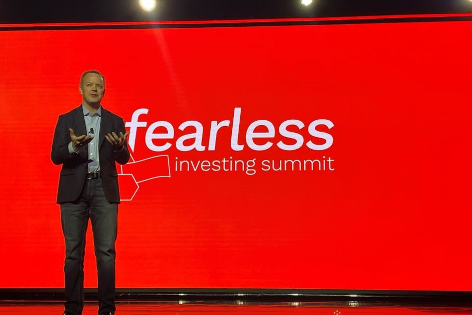 Riskalyze CEO Aaron Klein speaking in suit and red backdrop at Fearless Investing Summit